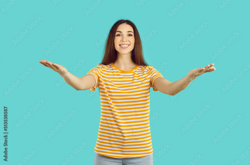 Smiling young woman isolated on blue studio background stand with open arms for hug or embrace. Happy female stretch hands to camera. Warm welcome or kindness concept.