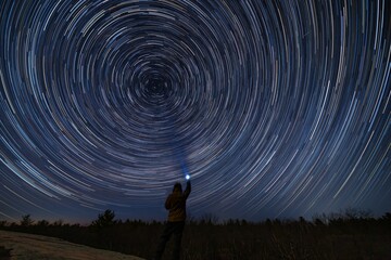 Wall Mural - person shining a light at the sky and making the stars rapidly move in circles - fantasy concept