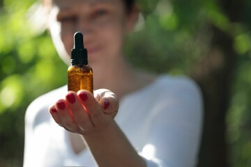 Female using cosmetic elixir in brown bottle. Copy space