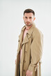 © GVS - Portrait of young trendy man in beige trench coat over white background
