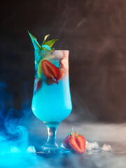 Wall Mural - strawberry summer cocktail with blue liqueur , smoky background with blue backlight