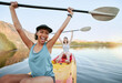 Portrait two diverse young woman cheering and celebrating while canoeing on a lake. Excited friends enjoying rowing and kayaking on a river while on holiday or vacation. Winning on a weekend getaway