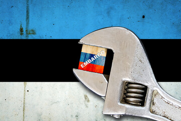 Embargo. Word on a wooden block in the colors of the Russian flag. Clamped wrench. Against the background of the flag of Estonia. Business. Politics.