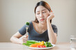 unhappy asian women is on dieting time looking at broccoli on the fork. girl do not want to eat vegetables and dislike taste