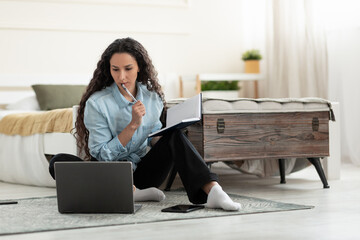 Poster - Lovely young woman writing in notebook during online lecture on laptop in bedroom, copy space. Web-based education
