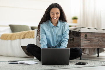 Poster - Beautiful young woman sitting on floor, working on laptop pc in bedroom, full length