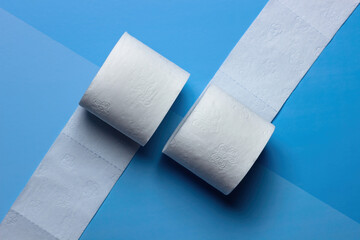 
Two rolls of toilet paper lie unwound in different directions on a blue and light blue background.  View from above