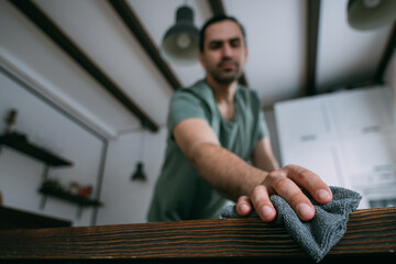 A young man is cleaning, dusting the table in the kitchen and living room at home.