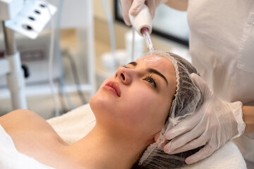 Wall Mural - Young woman receiving electric darsonval facial massage treatment at beauty salon.