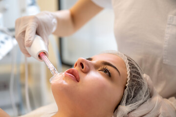 Wall Mural - Young woman receiving electric darsonval facial massage treatment at beauty salon. Close up