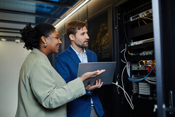 Portrait of two people in server room using laptop and setting up data security network