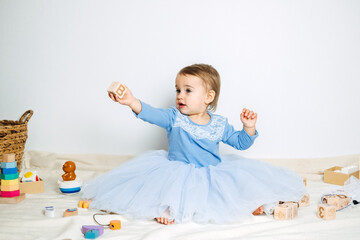 Wall Mural - Cute baby girl in blue princess dress playing with toys at home. Kids dresses for prom and birthday holiday