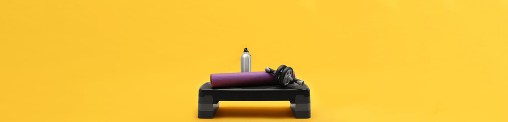 Wall Mural - Step platform, mat, bottle of water and abdominal wheel on yellow background. Banner design