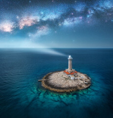 Wall Mural - lighthouse on smal island in the sea and milky way at night in summer. aerial view of beautiful ligh