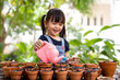 Adorable 3 years old asian little girl is watering the plant in the pots, concept of plant growing learning activity for preschool kid and child education for the tree in nature, montessori education.