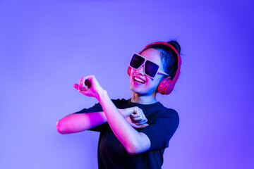 Young asian girl in black t-shirt wearing sunglasses and red headphones listen to music and dancing on purple background.
