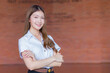 Portrait of adult Thai student in university student uniform. Asian beautiful girl standing smiling with her arms crossed on a brick background.