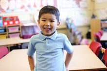 Young School Boy Standing In Front Of Desk, Smiling At Camera
