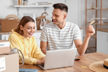 Poster - Young couple with laptop and credit card shopping online in kitchen