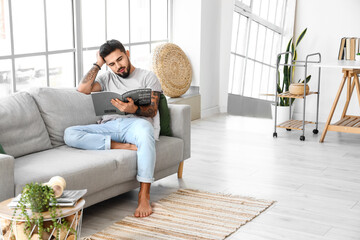 Poster - Handsome barefoot man reading magazine on sofa at home