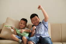 Excited Boy Singing Song Into Microphone When His Little Brother Playing Ukulele At Home