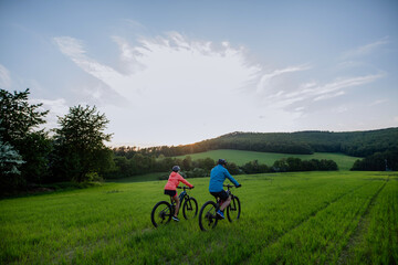 Wall Mural - Active senior couple riding electric bicycles on trail at summer park, healthy lifestyle concept. Rear view.