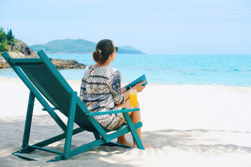 Wall Mural - Woman with book sits in sun lounger on beach and looks at sea on sunny day.