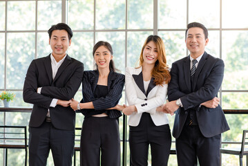 Portrait shot group of Asian happy cheerful millennial professional successful male businessman and female businesswoman in formal suit standing smiling cross hands holding together showing teamwork