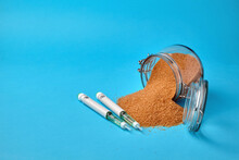 Insulin Syringe Pens And A Glass Jar With Scattered Brown Sugar On A Blue Background With Copy Space