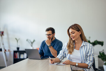 Two focused people working at the office, a woman making plans, and a man using a laptop.