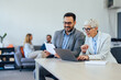 © bnenin - Close up of business colleagues working together, a mature female using a laptop, and an adult man reading some documents.