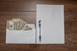 Envelope with dollars, a blank sheet of paper and a pen on a wooden table. The concept of arrest, interrogation, frank confession. Punishment for bribery.