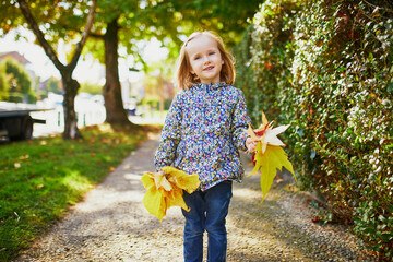 Adorable preschooler girl enjoying nice and sunny autumn day outdoors