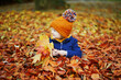 Adorable preschooler girl sitting on the ground in large heap of fallen leaves and playing with them on autumn day