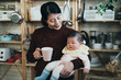 portrait loving asian new mother is looking at her adorable newborn child in arm with a smile while holding and having coffee in a cozy kitchen at home.