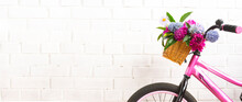 Pink Bicycle With A Basket Of Flowers Against A Brick Wall