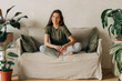 © Ilona - Portrait of a cheerful happy young female brunette sitting cross-legged on the sofa.