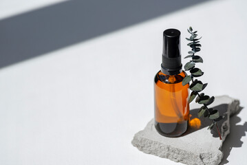 Wall Mural - Amber pump bottle with serum, tonic or essential oil on grey concrete podium with eucalyptus branches. White background with daylight. Beauty concept for face and body care