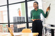 © Vadim Pastuh - Confident african-american female employee standing near whiteboard and points on it, explains something to online audience on the laptop, conducts online conference, presentation, video meeting