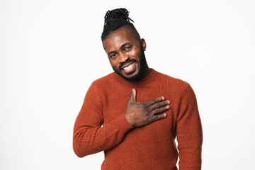 Cheerful touched with a compliment happy shy african-american young man in red sweater with dreadlocks looking at camera with toothy smile isolated in white background