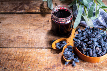 Wall Mural - Small glass jar with homemade  haskap berry jam, on wooden background with bowl of fresh haskap (honeysuckle, honeyberry) berries, copy space