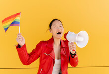 Happy Woman Holding Rainbow Flag Shouting Through Megaphone In Front Of Yellow Wall