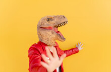 Playful Woman Wearing Dinosaur Mask Against Yellow Background