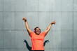 © VISTA by Westend61 - Cheerful woman with arms raised enjoying music in front of wall on sunny day