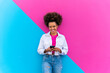 © VISTA by Westend61 - Smiling young woman with mobile phone standing in front of pink and blue wall