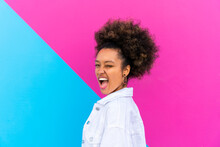Afro Woman With Mouth Open Winking Eye In Front Of Pink And Blue Wall