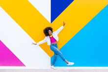 Smiling Young Woman With Arms Outstretched In Front Of Colorful Wall