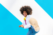 Happy Young Afro Woman Kicking In Front Of Blue And White Wall