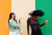 Cheerful Women Enjoying Dance In Front Of Multi Colored Wall