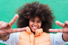 Smiling Girl Gesturing Peace Sign In Front Of Wall